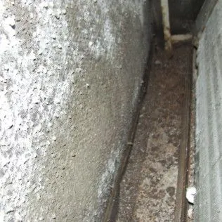 Narrow dirty alley between concrete walls, with debris and a small pipe opening at the end.